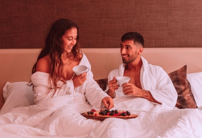 Casal de robe branco na cama com chávenas e tábua de frutas