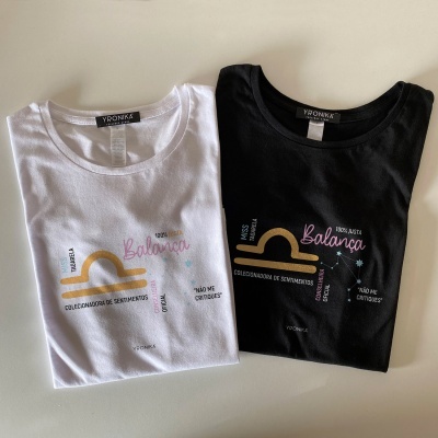 Duas t-shirts dobradas, branca e preta, com estampas coloridas e texto visível.