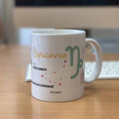Caneca branca com símbolo e texto do signo Capricórnio em várias cores