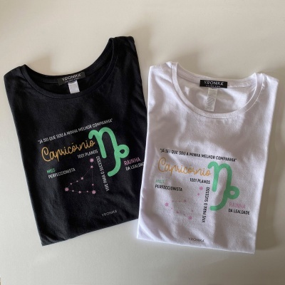 Duas t-shirts, preta e branca, com desenho do signo Capricórnio