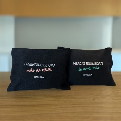 Duas bolsas pretas com texto bordado colorido em cima de uma mesa de madeira clara.