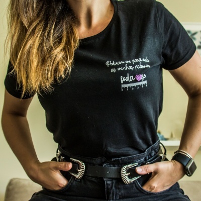 T-shirt preta de manga curta com texto bordado na frente usada por pessoa