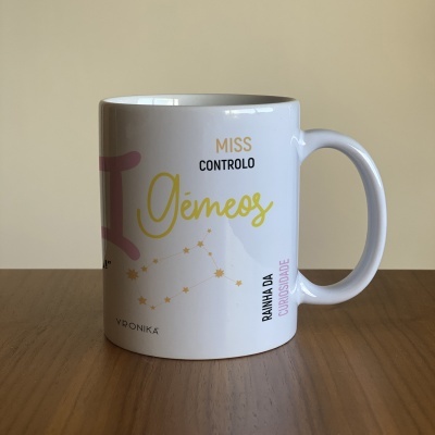 Caneca branca com design do signo Gémeos e texto em português.