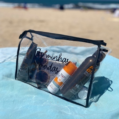 Bolsa transparente com produtos de proteção solar sobre tecido azul na praia