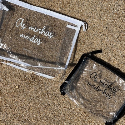 Dois sacos transparentes com textos distintos numa superfície de areia.