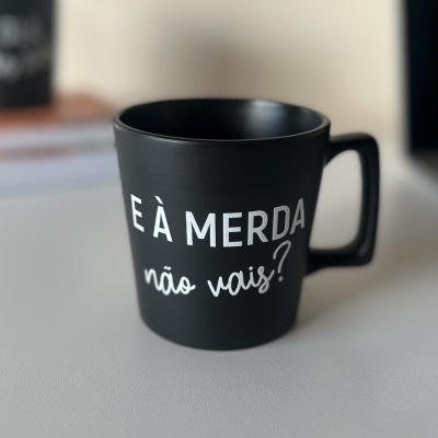 Caneca preta com frase em branco e pega na direita sobre superfície branca