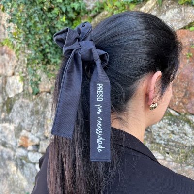 Elástico preto para cabelo com fita de texto branco PRESO por necessidade, cabelo preto e parede de pedra com trepadeiras.