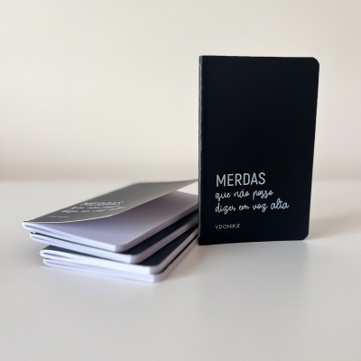 Cadernos pequenos com capas preta e cinza, texto branco, sobre superfície branca