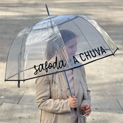 Mulher com casaco bege a segurar guarda-chuva transparente com texto preto