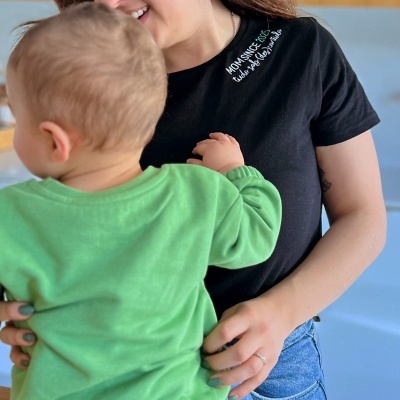 Camiseta preta com texto bordado MOM SINCE 2023 e mulher a segurar bebé de casaco verde