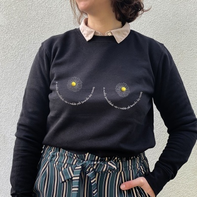 Camisola preta com estampa de flores e texto, usada com camisa bege e calças às riscas.