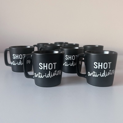 Conjunto de chávenas pequenas pretas com texto branco 'SHOT anti-idiotas'