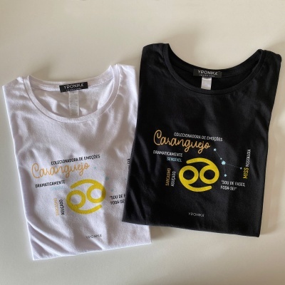 Duas t-shirts, branca e preta, com estampa do signo caranguejo e texto alusivo.