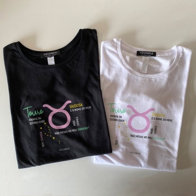 Dois T-shirts, um preto e outro branco, com estampas coloridas e textos em português com símbolo de touro