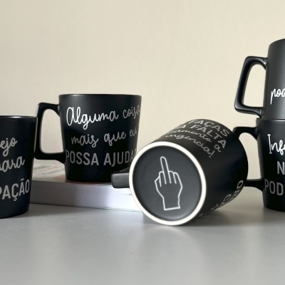 Seis canecas pretas com texto branco em português e uma ilustração de mão, dispostas sobre uma superfície branca.