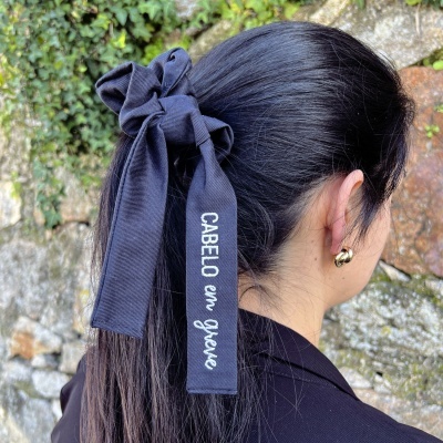 Elástico de cabelo preto com fita bordada com texto branco usado em cabelo escuro