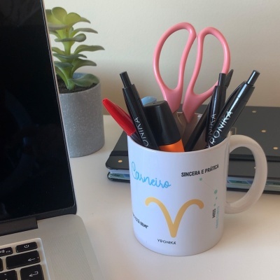 Caneca branca com texto e símbolo de signo usada para guardar material de escritório