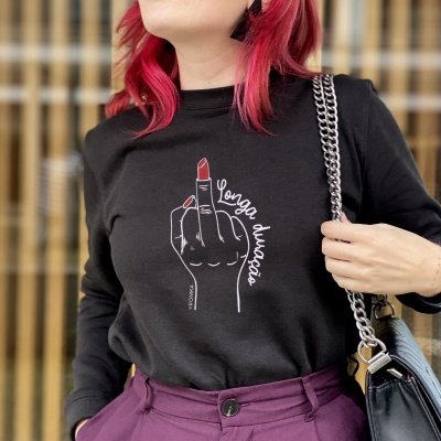 Pessoa a usar t-shirt preta com ilustração e texto, calças roxas e bolsa preta com alça de corrente