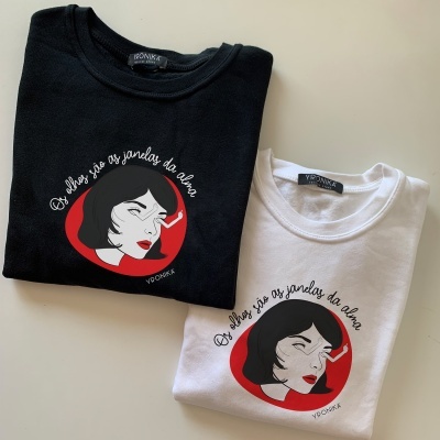 Duas t-shirts dobradas, preta e branca, com estampa de rosto feminino e texto em português