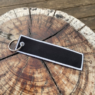 Chaveiro retangular preto com borda branca sobre tronco de árvore