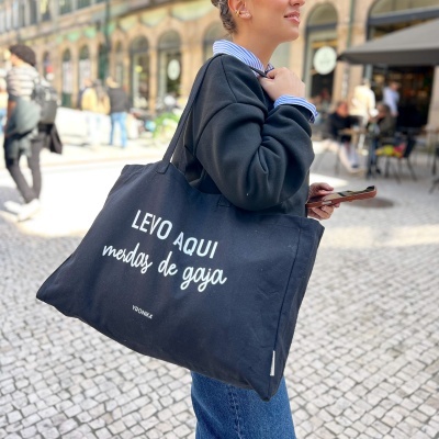 Pessoa a segurar saco de pano preto com texto em branco num ambiente urbano.