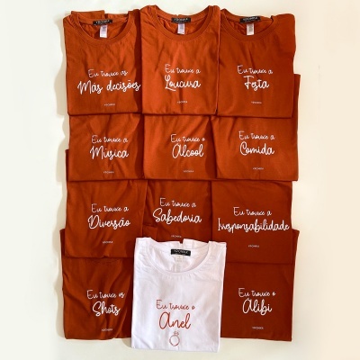 Dez T-shirts dobradas com frases em português, nove laranja e uma branca, exibidas sobre fundo branco.