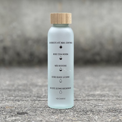 Garrafa de vidro translúcida com tampa de madeira e texto em português