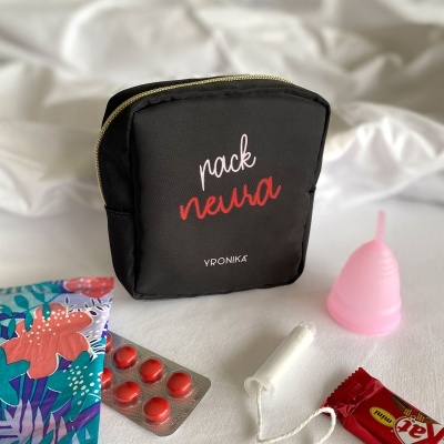 Bolsa preta com texto e vários produtos menstruais sobre tecido branco