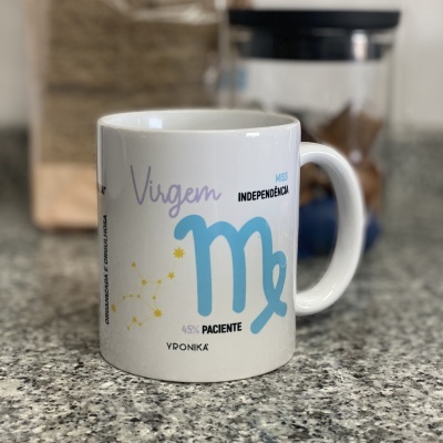 Caneca branca com símbolo de Virgem e texto em cores azul e roxo sobre bancada de granito cinzento