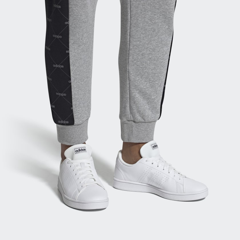 Ténis brancos adidas com calças de treino cinzentas com faixa preta e logotipo adidas.