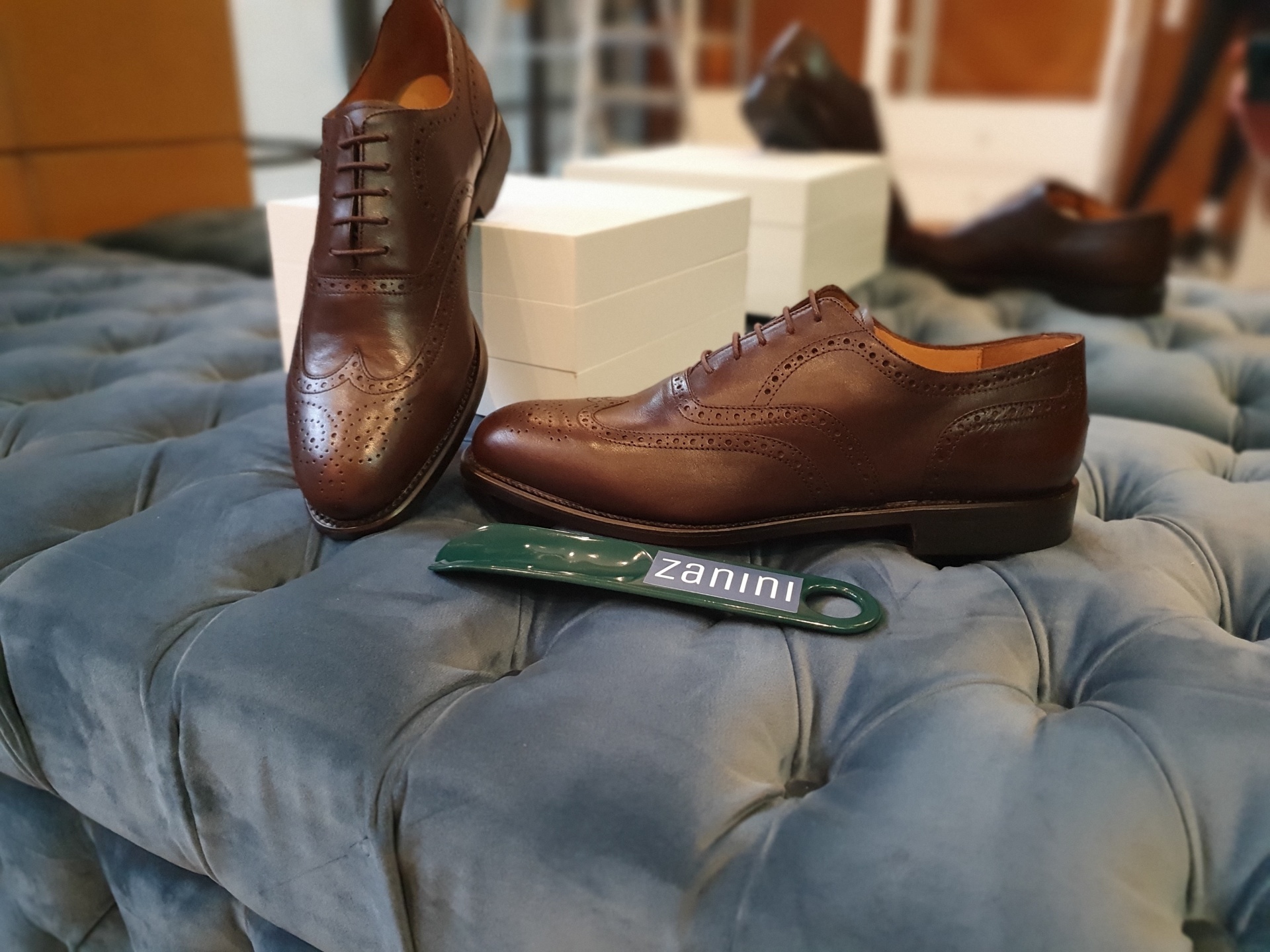 OXFORD WING TIP CASTANHO Par de sapatos castanhos de couro com padrão brogue sobre estofado azul com caixas e espátula zanini.