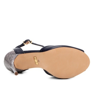 Sandália de salto fino preta com sola bege vista pela parte inferior, salto riscado preto e branco e fivela dourada
