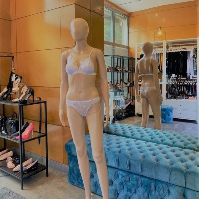 Mannequin with white lace lingerie in boutique with golden walls, blue bench, shoes and bags on shelves