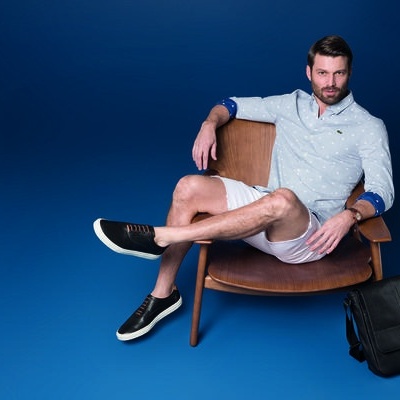 Homem sentado em cadeira de madeira com mochila preta ao lado