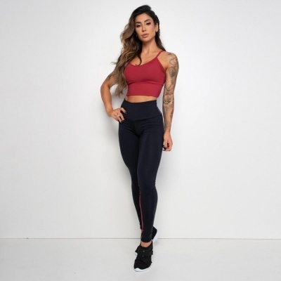 Mulher a usar roupa desportiva vermelha e preta de pé contra parede branca