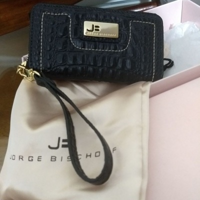 Carteira preta de pele croco com placa metálica e bolsa creme com logótipo dentro de caixa rosa