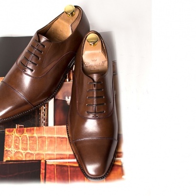 Sapatos sociais masculinos castanho escuro em couro liso sobre caixa preta com padrão de couro de crocodilo.