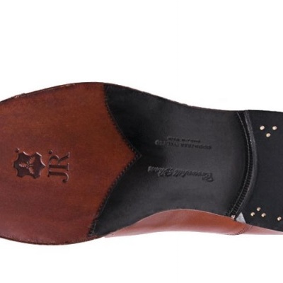 Sola de sapato em couro castanho com pregos metálicos e marca gravada.