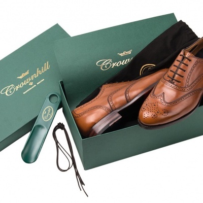 Sapatos de pele castanhos dentro de caixa verde da marca Crockfield com escova para sapatos