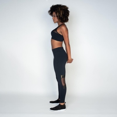 Mulher em perfil com roupa desportiva preta e ténis pretos com sola branca em fundo branco