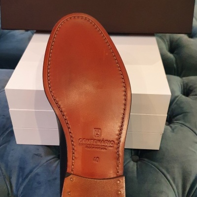 Sola de sapato de couro castanho com selo Centenário e caixa de sapatos castanha ao fundo