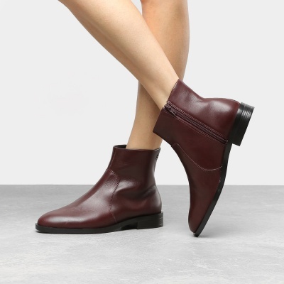 Botas de couro castanho escuro com fecho lateral e sola preta, em fundo cinzento.