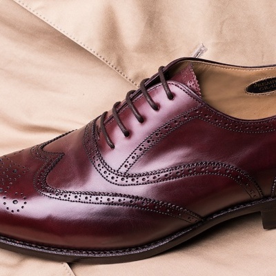 Sapato social masculino em couro vinho e castanho com padrão clássico, sobre tecido bege