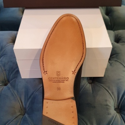 Sola de sapato castanha com estampagem Centenário, caixas brancas e caixa castanha ao fundo