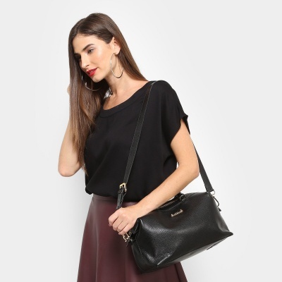 Mulher com blusa preta e saia vinho segurando bolsa preta em fundo branco