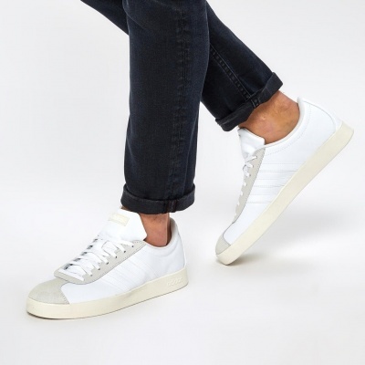 Ténis brancos com detalhes cinzentos claros usados com calças pretas dobradas