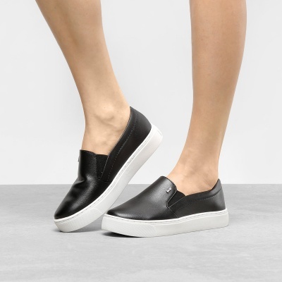 Sapatilhas slip-on pretas com sola branca em fundo cinza