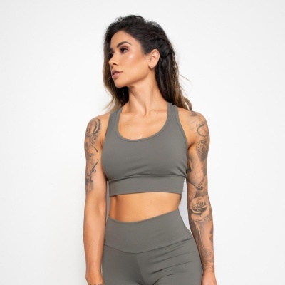 Mulher com roupa desportiva cinzenta e tatuagens nos braços, em fundo branco