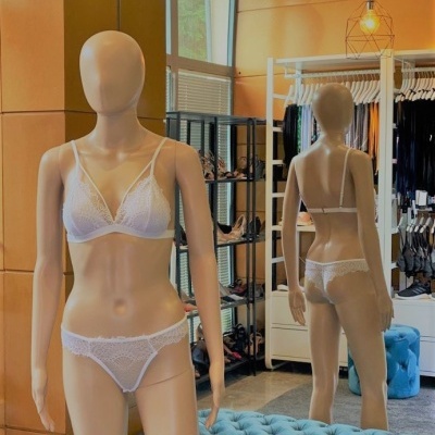 Mannequim com conjunto de lingerie branca de renda em loja com paredes bege e banco azul