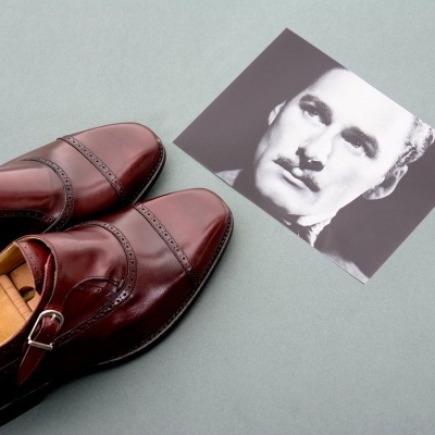 Sapatos de couro castanho com fivela ao lado de fotografia preto e branco de homem